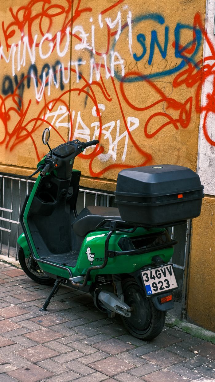 Vibrant green scooter against colorful graffiti wall on urban street, showcasing street art culture.