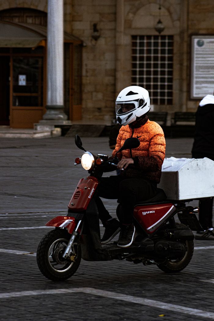 A motor scooter rider in helmet drives through a historic city square, blending modern transport with vintage architecture.